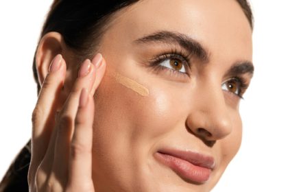 close up of young woman with soft skin applying makeup foundation on cheek with fingers isolated on