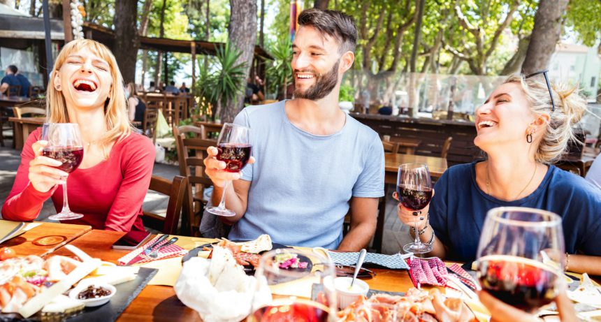 Millenial people having fun drinking red wine glasses at lunch party on sunny day